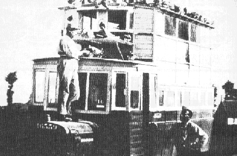 Photographie ancienne d’un véhicule à deux niveaux aménagé en colombier, avec des pigeons sur le toit.